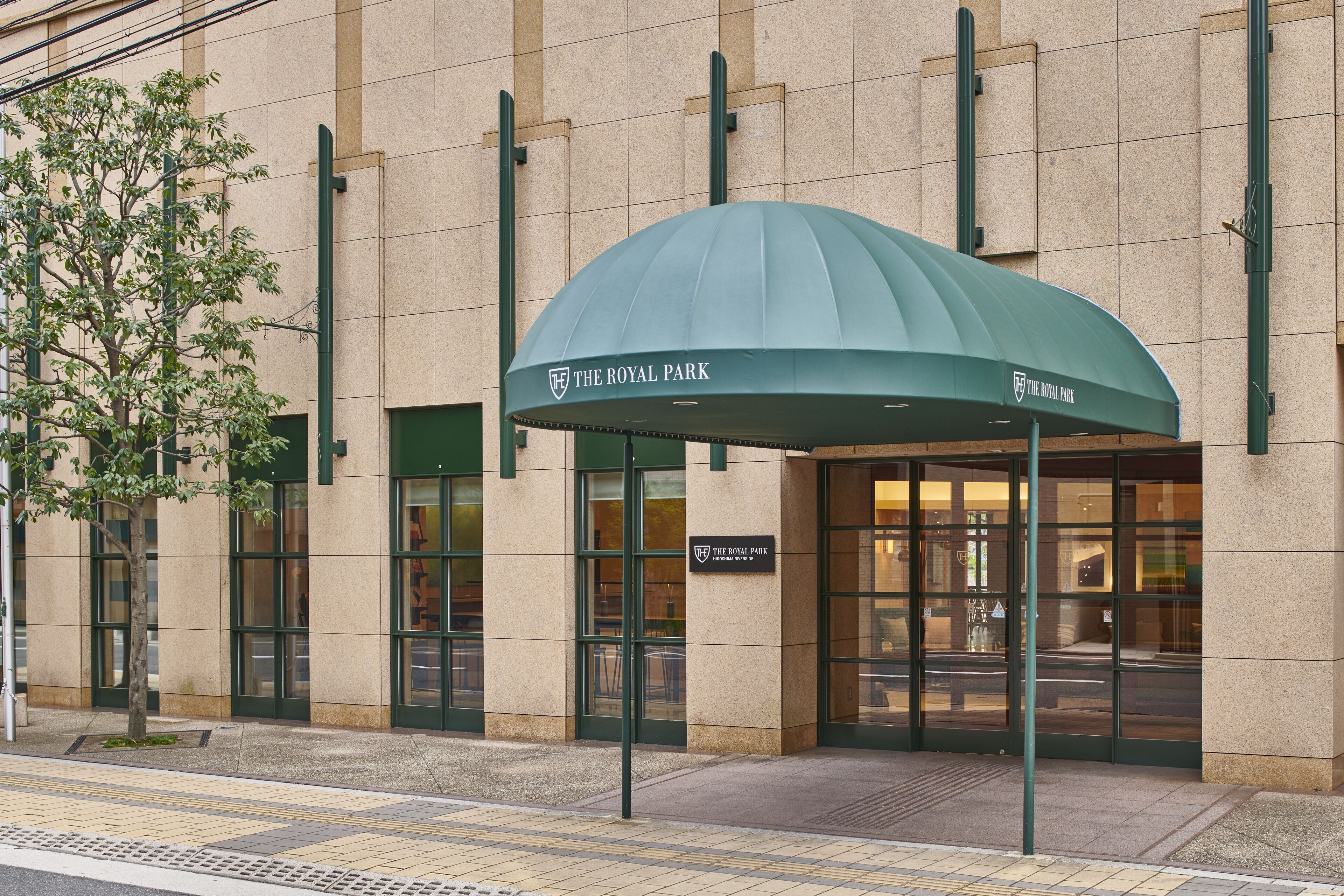 The entrance of The Royal Park hotel with a green awning, large glass doors, and a sign above the entrance.