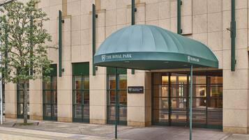 The entrance of The Royal Park hotel with a green awning, large glass doors, and a sign above the entrance.
