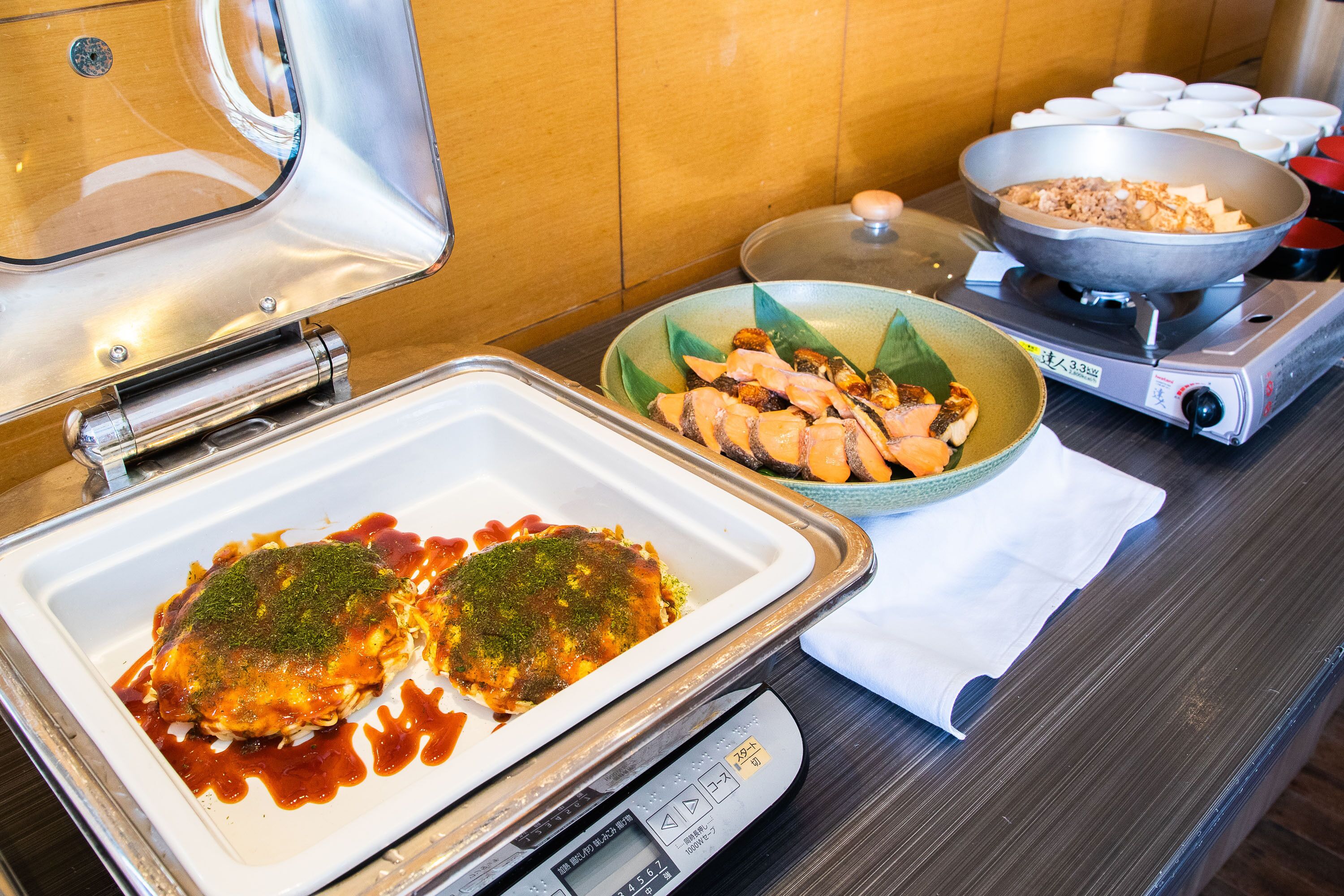 A buffet table with a variety of dishes, including a large bowl of rice, a plate with two pieces of food covered in sauce, and a bowl of sliced meat.