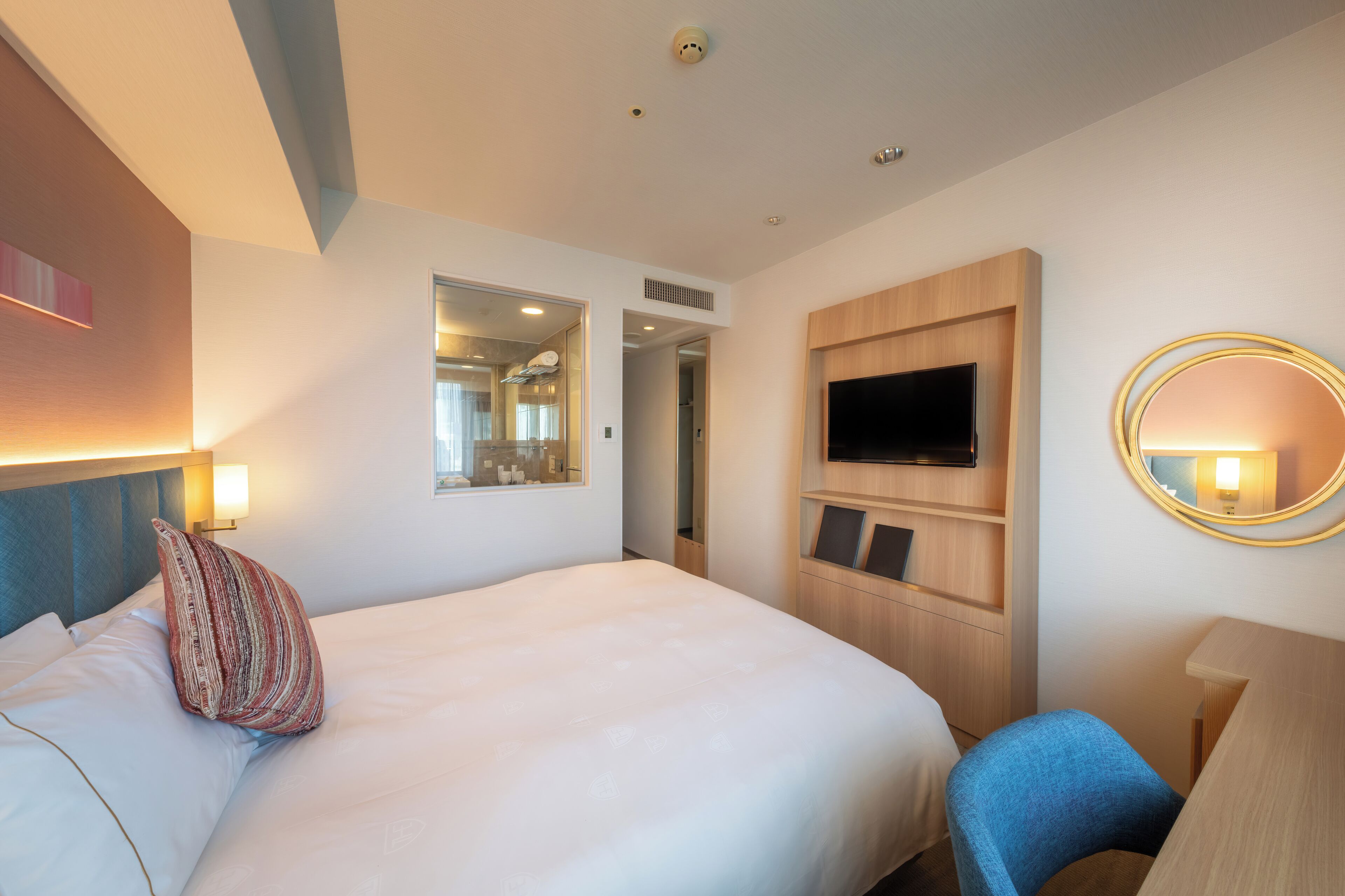 A hotel room with a bed, a TV, a mirror, and a desk.