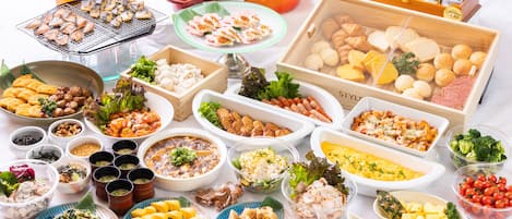 A variety of food items and beverages on a table, including grilled fish, dumplings, sausages, and a selection of pastries and bread.