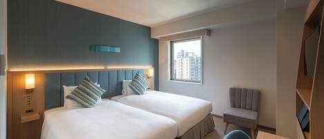 A hotel room with two beds, a small table, a chair, a TV, and a window with a city view.