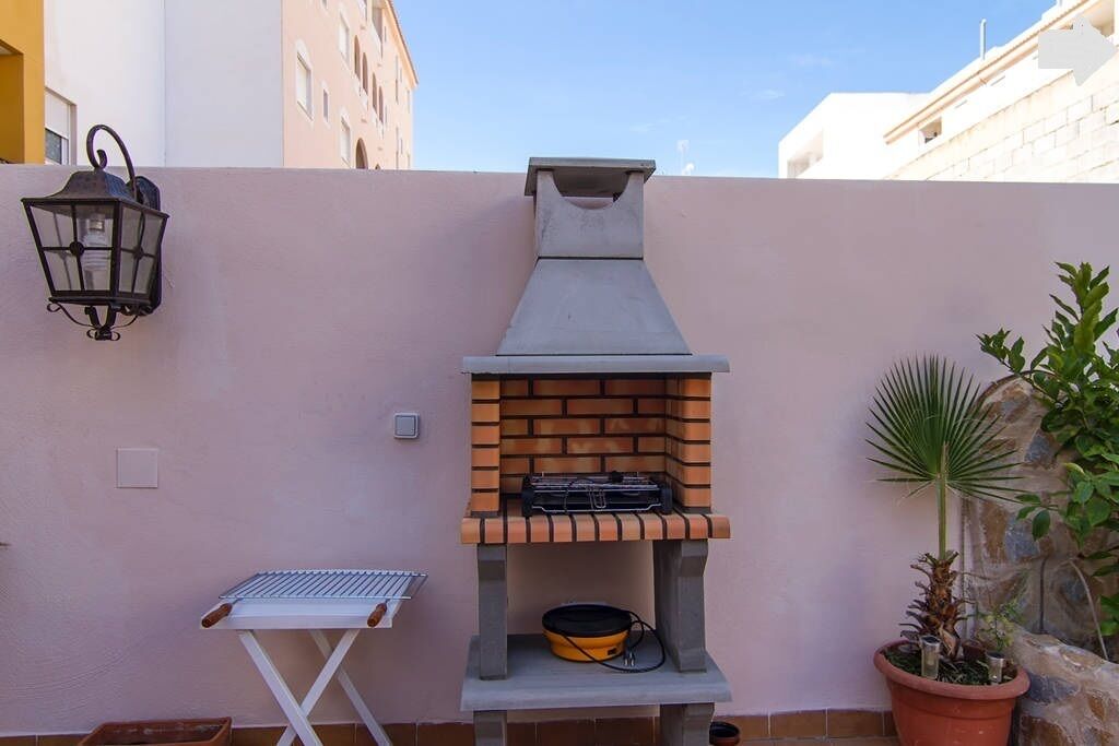 Un barbecue extérieur en briques, doté d’une cheminée, d’une petite table et d’une plante en pot.