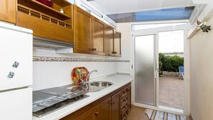 A compact kitchen with wooden cabinets, a stainless steel sink, and a glass door leading to a patio. - cozy apartment with 140m terrace with private pool (Torrevieja)