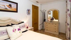 A bedroom with a bed, a dresser, a mirror, and a painting on the wall. - cozy apartment with 140m terrace with private pool (Torrevieja)