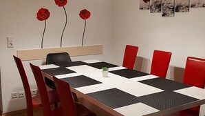 Un comedor con una mesa blanca, sillas negras y rojas, y una lámpara en el techo.
