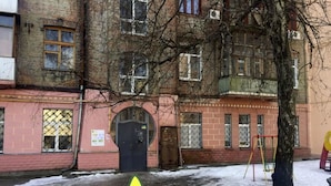 Un immeuble à plusieurs étages, doté d’une façade rose, d’une porte noire et d’une flèche jaune pointant vers le haut.