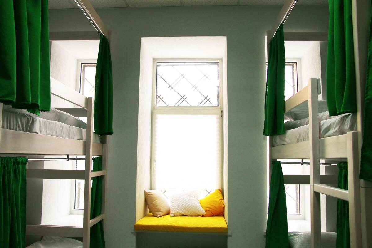 Un dormitorio con literas, una ventana con cortinas verdes y una almohada amarilla en la cama inferior.