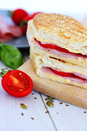 A sandwich with visible layers of ham, cheese, and tomato, placed on a wooden cutting board.