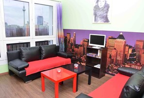 A living room with a black leather sofa, a red table, and a cityscape mural on the wall.