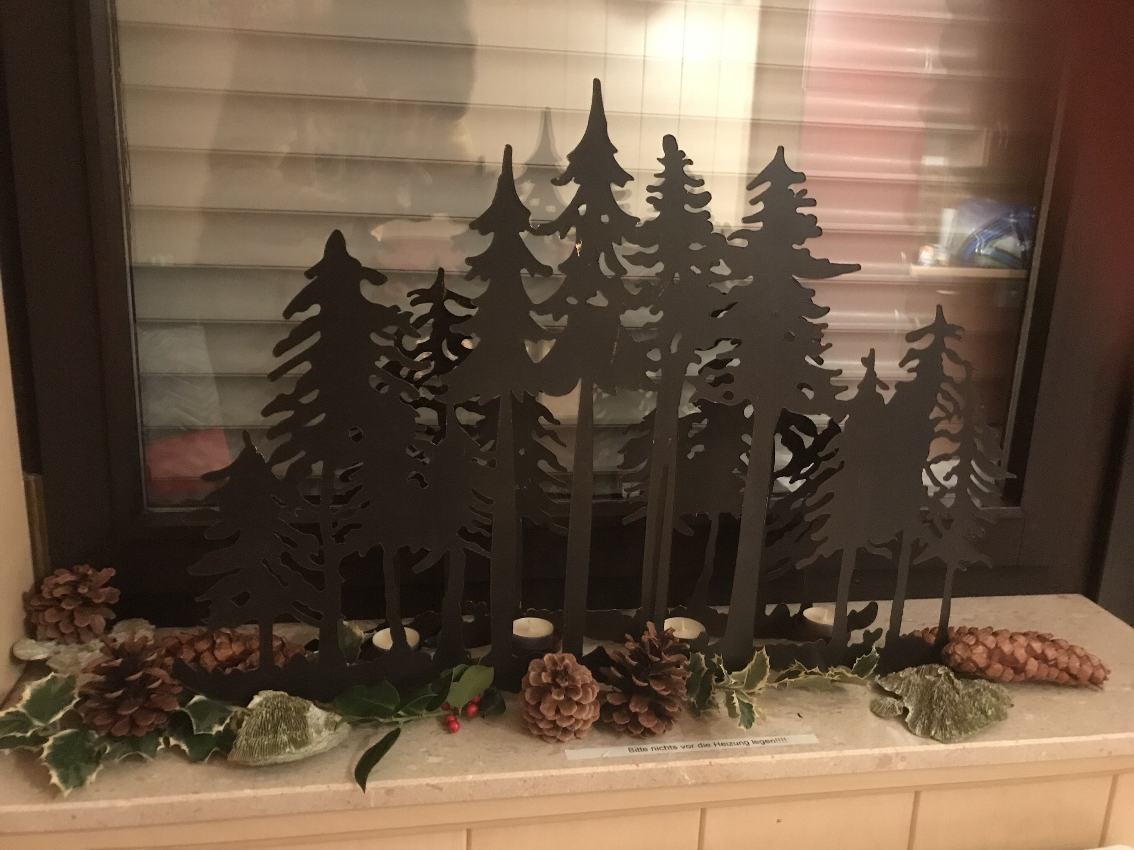 A window display with a silhouette of evergreen trees, pinecones, and holly leaves.