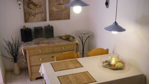 Un comedor con una mesa dispuesta para cuatro personas, sillas de madera, un cuenco decorativo con frutas y un florero con ramas.