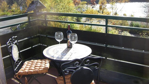 Un balcón con una mesa, dos copas de vino y una botella.