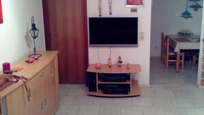 Una sala de estar con un televisor montado en la pared, un mueble de madera, un reloj y un cuadro enmarcado.