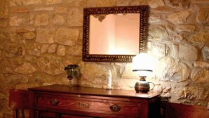 A wooden dresser with a mirror and a lamp against a stone wall. - Agriturismo Santa Maria (San Venanzo)