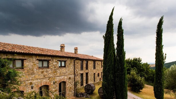 A stone building with a tiled roof, two tall cypress trees, and a gravel path. - Agriturismo Santa Maria (San Venanzo)