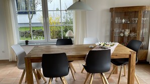 A dining area with a wooden table, black chairs, a glass cabinet with china, and a view of the outdoors through large windows. - Cottage on the mountain (Strohn)