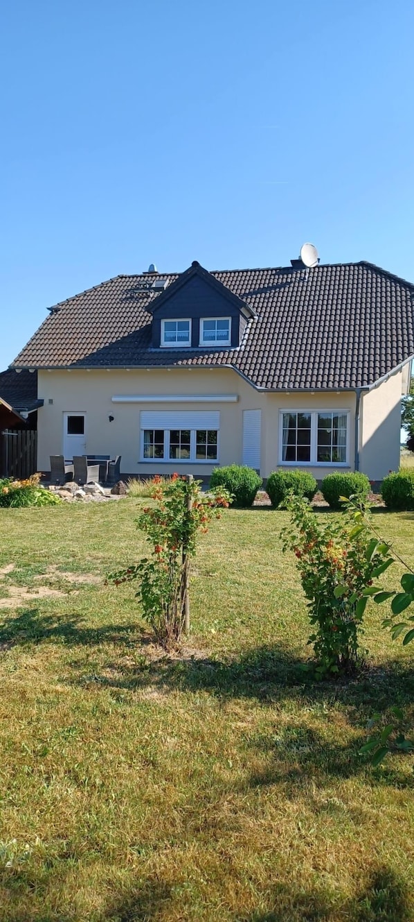 Une maison à deux étages, avec un toit recouvert de tuiles, une antenne parabolique et une pelouse bien entretenue agrémentée de petits arbustes.