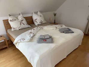 Un lit bien fait, avec un oreiller orné d’un motif de feuilles, une serviette pliée et une lampe de chevet.
