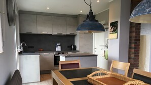 A modern kitchen with stainless steel appliances, a dining area with a wooden table and chairs, and a hanging light fixture.