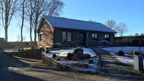 A two-story brick house with a sloped roof, a fenced driveway, and snow on the ground.