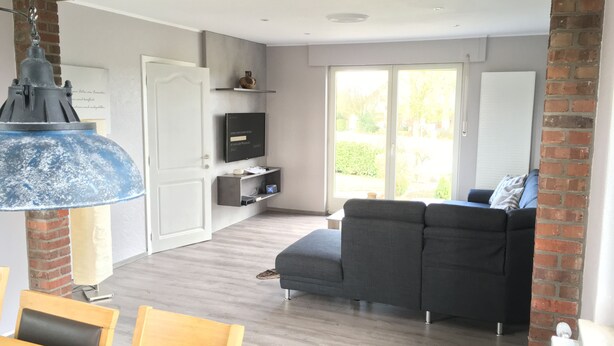 A modern living room with a grey sofa, wooden dining table, and a TV on a shelf.