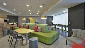 Un área de descanso moderna con un sofá verde, una mesa amarilla y sillas rojas.
