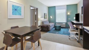 Una habitación de hotel moderna con comedor, sofá, televisión y un ventanal grande.