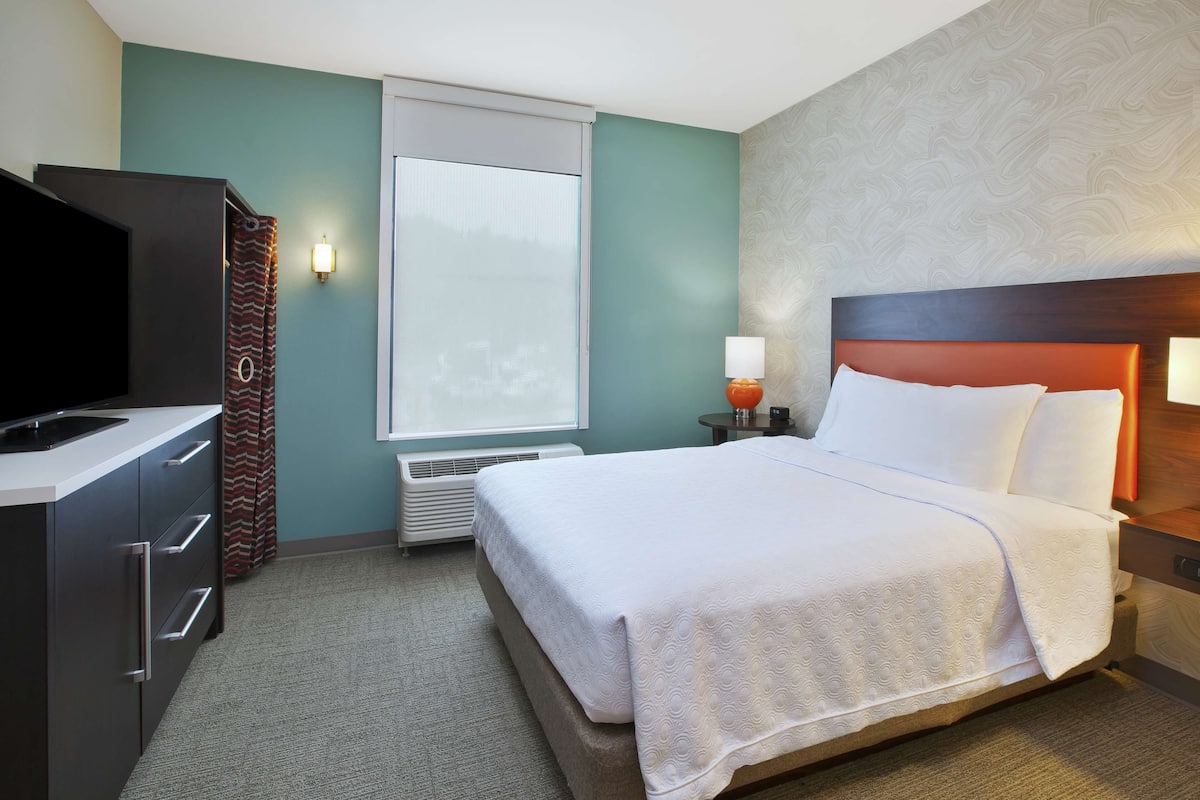 Een hotelkamer met een bed, een televisie, een verwarming en een raam met gordijnen.