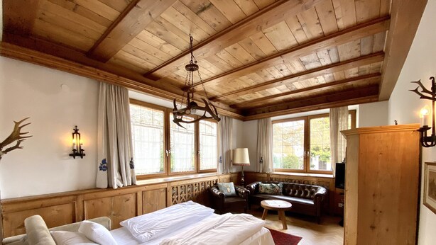 A bedroom with a large bed, wooden ceiling beams, a sofa, and a window with curtains.