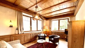 A cozy living room with a wooden ceiling, a sofa, two armchairs, a small table, and a red rug.
