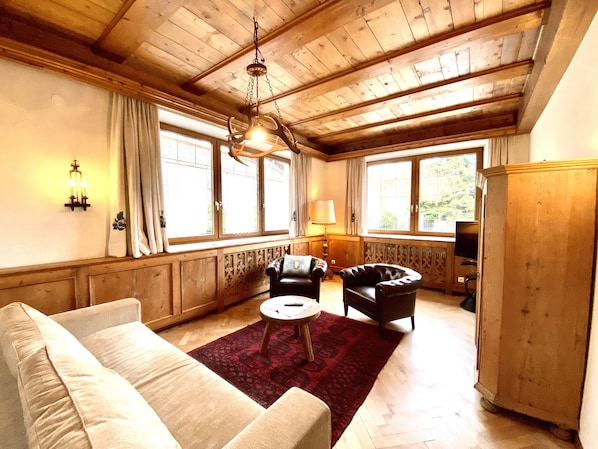 A cozy living room with a wooden ceiling, a sofa, two armchairs, a small table, and a red rug.