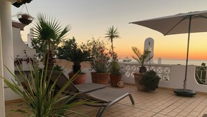 Une terrasse avec un fauteuil de relaxation, des plantes en pot et un parasol.