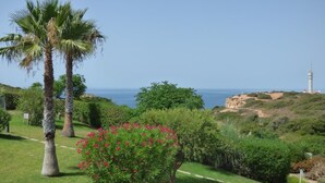 Un paysage côtier avec des palmiers, un ciel dégagé et un phare à l’horizon.