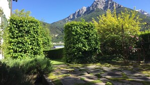 En trädgård med stenlagda gångar, frodig grönska och en bergskedja i bakgrunden.