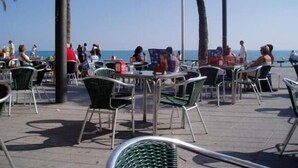 Un'area salotto all'aperto con tavoli e sedie, palme e vista sul mare.