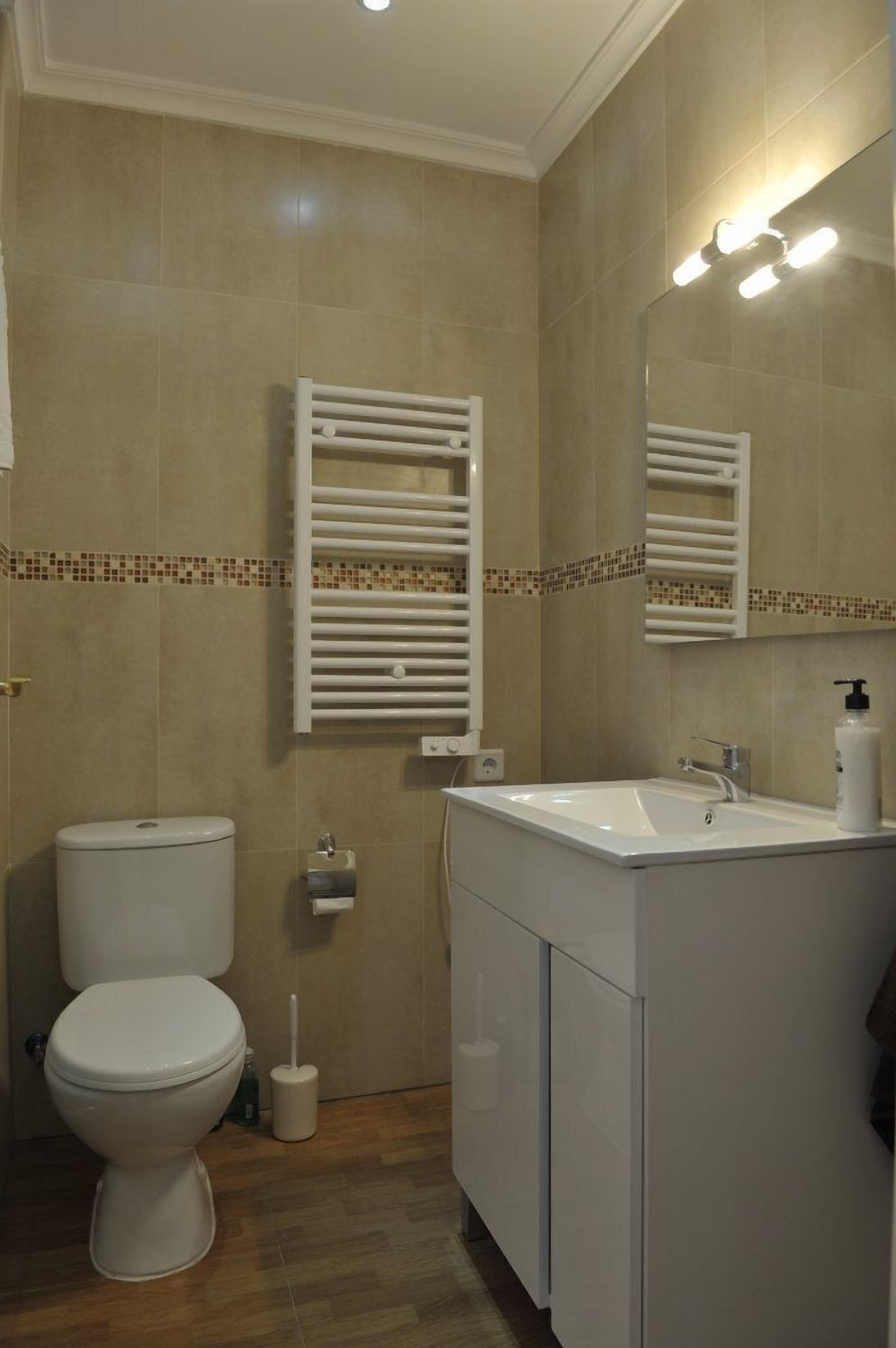 Un baño con inodoro, lavamanos y perchero para toallas.