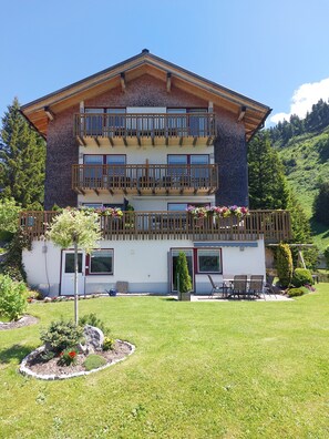Un immeuble de deux étages doté de balcons, d’un jardin et surplombant un paysage montagneux.