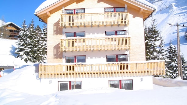 A multi-story building with balconies, surrounded by snow-covered trees and a clear sky.