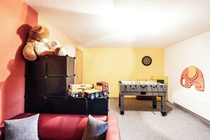 A cozy room with a red sofa, a teddy bear, a foosball table, and a dartboard. - New, free WiFi, garden, lawn, playground, beautiful mountain backdrop,  (Schröcken)
