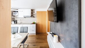 A modern kitchen with white cabinets, a wooden dining table, and a flat-screen TV mounted on the wall.