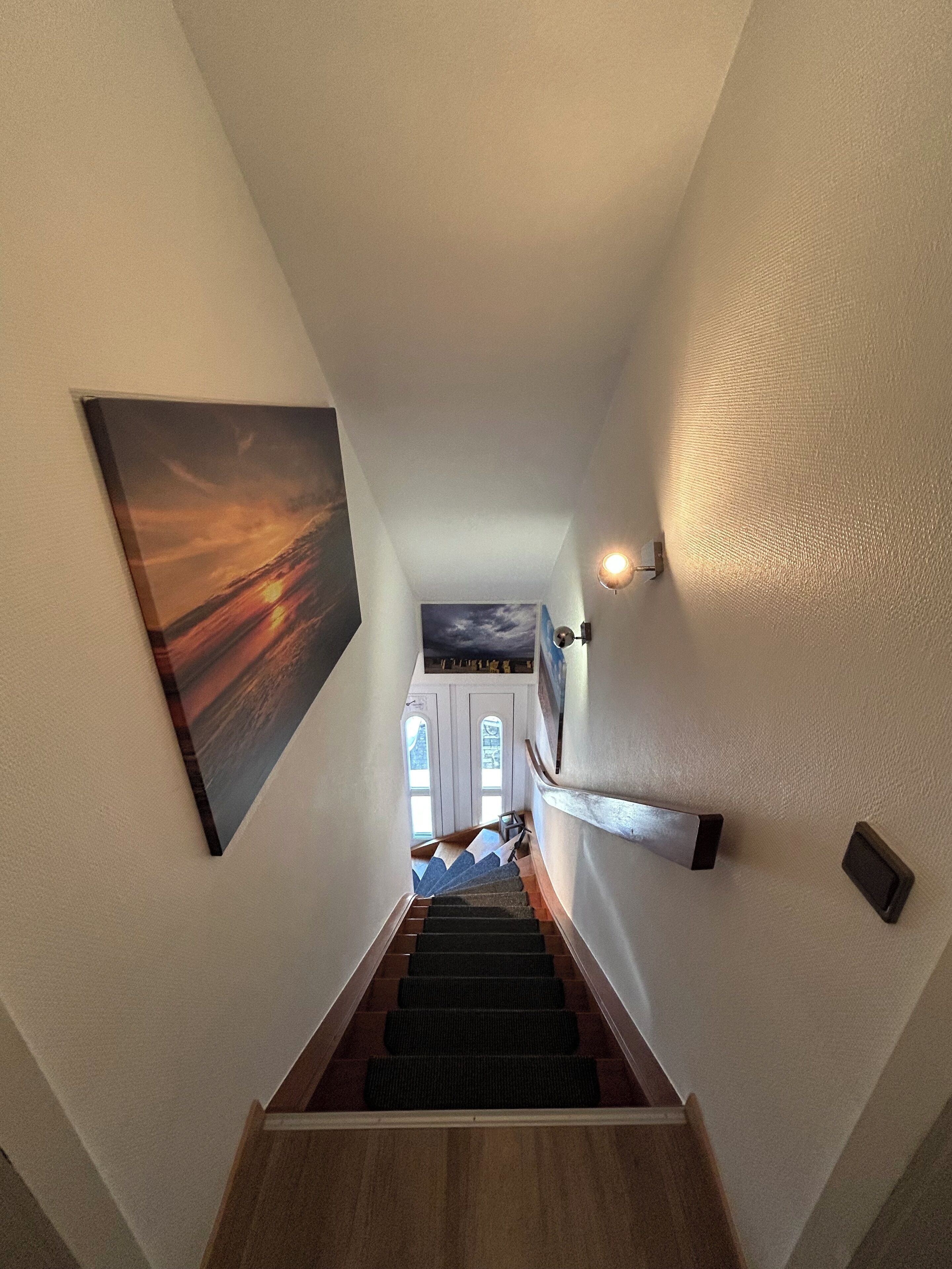 A staircase with a handrail, a wall-mounted light fixture, and a framed picture.
