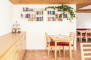 Un coin repas avec des tables et des chaises en bois, une bibliothèque remplie de livres et une plante.