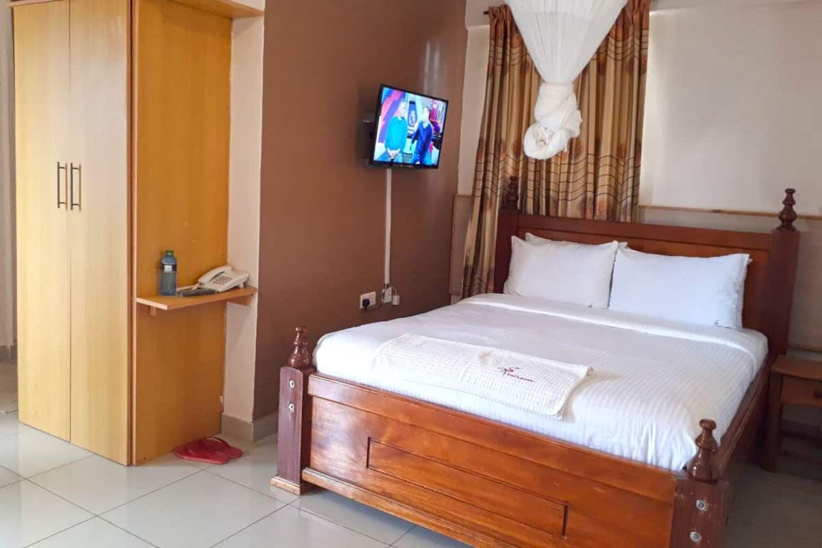 A bedroom with a wooden bed, a television on the wall, a wardrobe, and a bedside table.