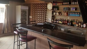 A bar area with a long counter, stools, and shelves stocked with bottles. - Hôtel Le Premier (Kisii)