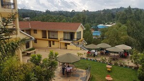 A courtyard with outdoor seating, a building with a tiled roof, and surrounding greenery. - Hôtel Le Premier (Kisii)