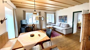 Une pièce chaleureuse avec un plafond en bois, une table à manger recouverte d’une nappe blanche, un canapé et un téléviseur.