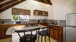 A kitchen with a central island, wooden cabinets, a stainless steel refrigerator, and a window with a view of greenery. - Apartment La Batie self catering for 2 on Beau Vallon (Mahe)