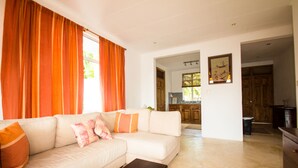 A living room with a sofa, a coffee table, and a kitchen visible through an open doorway. - Apartment La Batie self catering for 2 on Beau Vallon (Mahe)