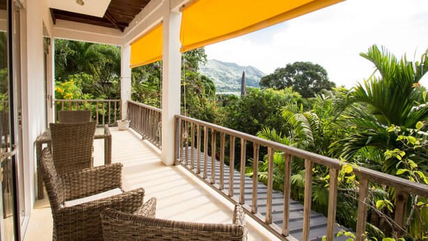 A covered balcony with wicker furniture, a view of lush greenery and mountains. - Apartment La Batie self catering for 2 on Beau Vallon (Mahe)